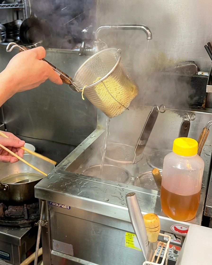 茹で上がった麺の入ったザルを力強く振り、水分を切っている様子。