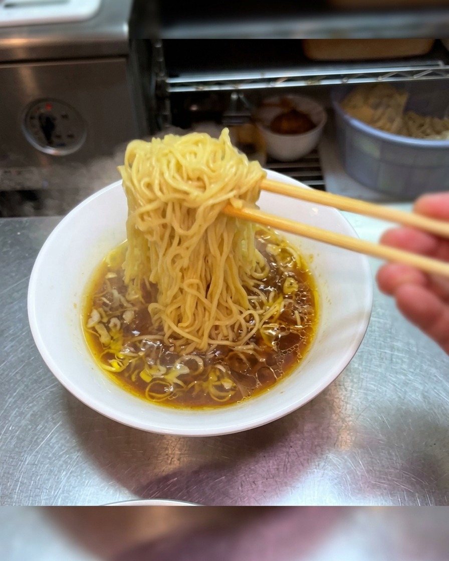 箸で麺を持ち上げ、スープの中で綺麗に整えながら盛り付けている様子。