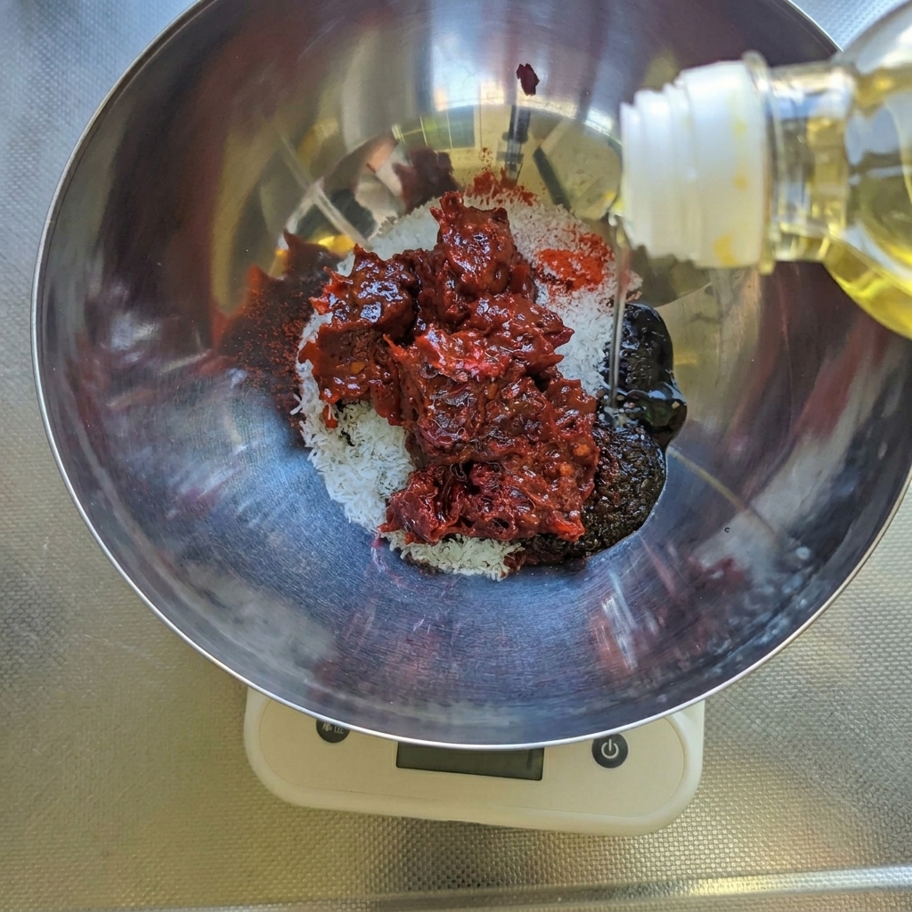 粉唐辛子の入ったボウルに、甜麺醤、豆板醤、サラダ油などの調味料を加えている様子。