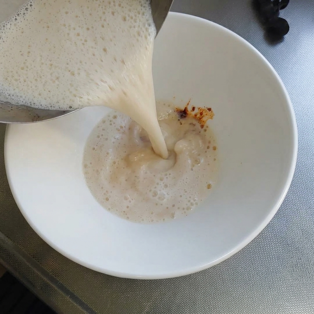 手鍋から沸騰直前の白濁したとんこつスープを、調味料の入った丼に注いでいる様子。