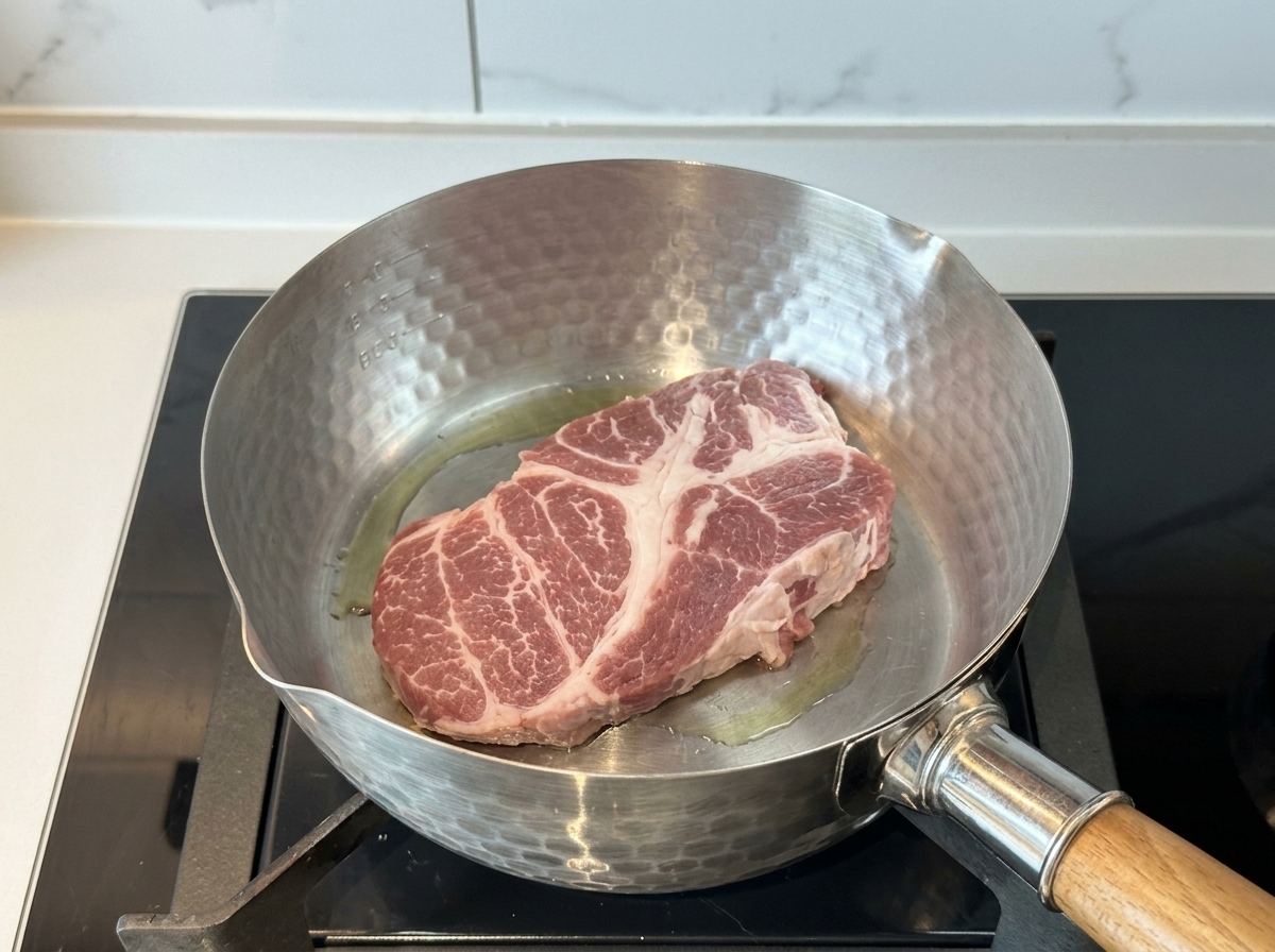 油を引いた鍋で、厚切りの豚肩ロースを焼いている様子。