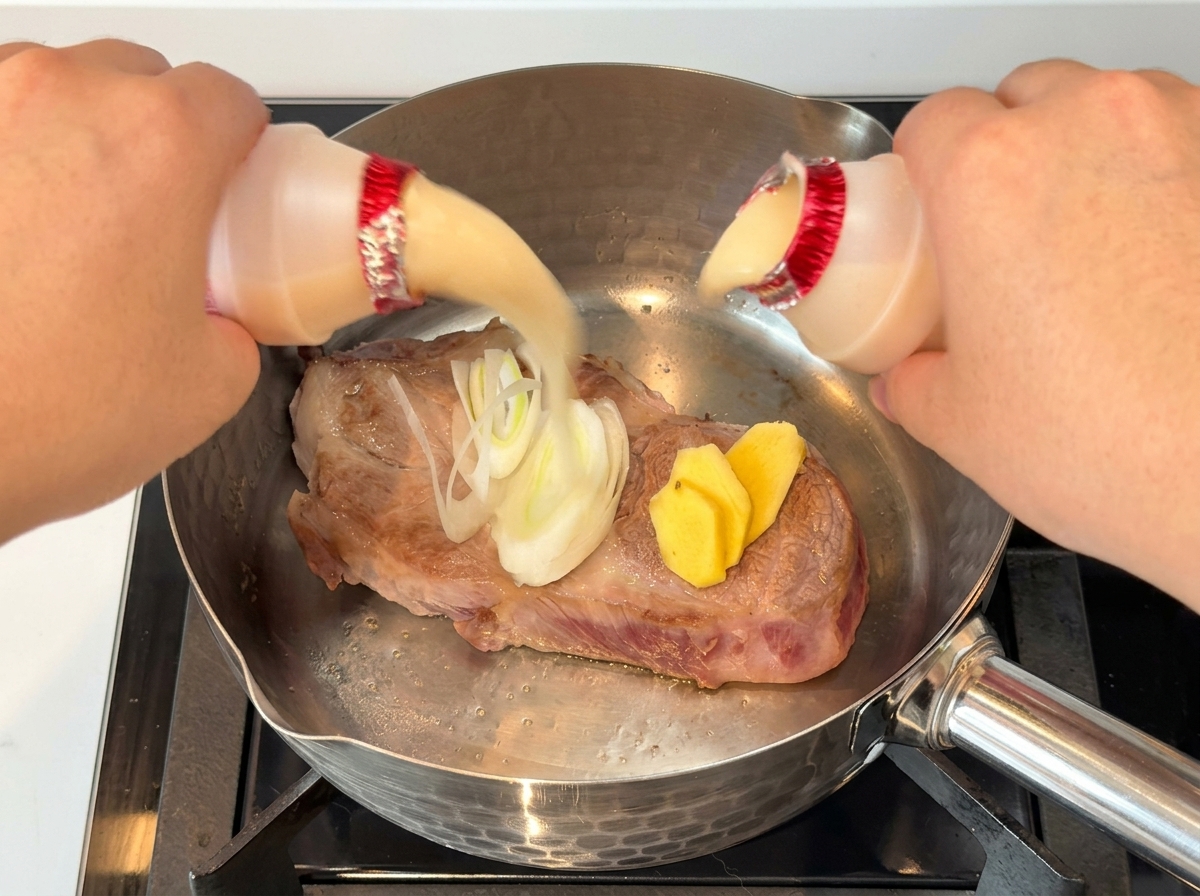 焼いた豚肉に、小さなボトルの乳酸菌飲料を2本注いでいる様子。