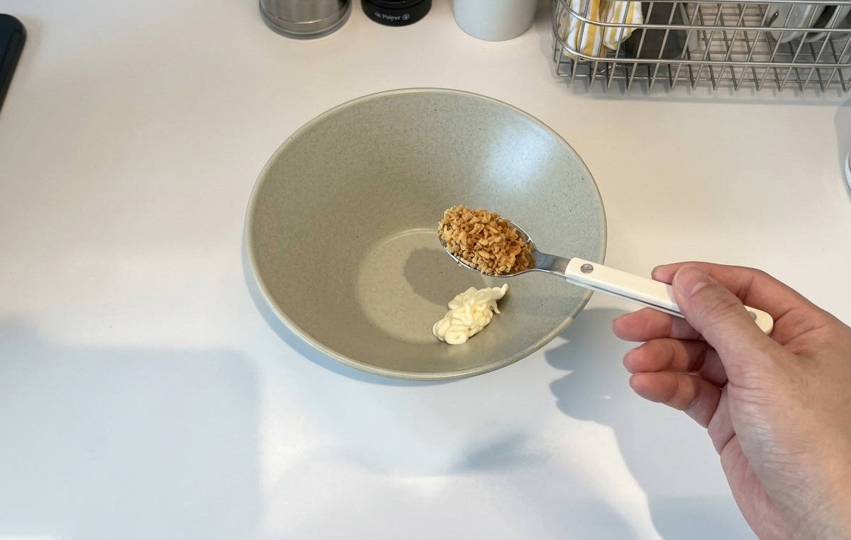 丼の中のマヨネーズの上に、フライドガーリックをスプーンで乗せる様子。