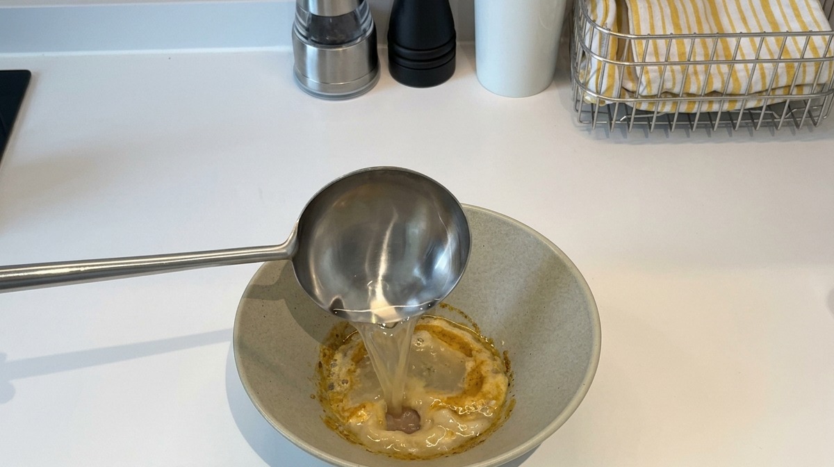 ペーストの入った器に、お玉で熱いゆで汁を注いでいる様子。