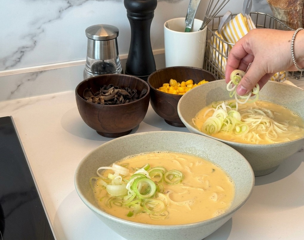 器に盛られたラーメンに、刻みねぎをたっぷりと散らしている様子。