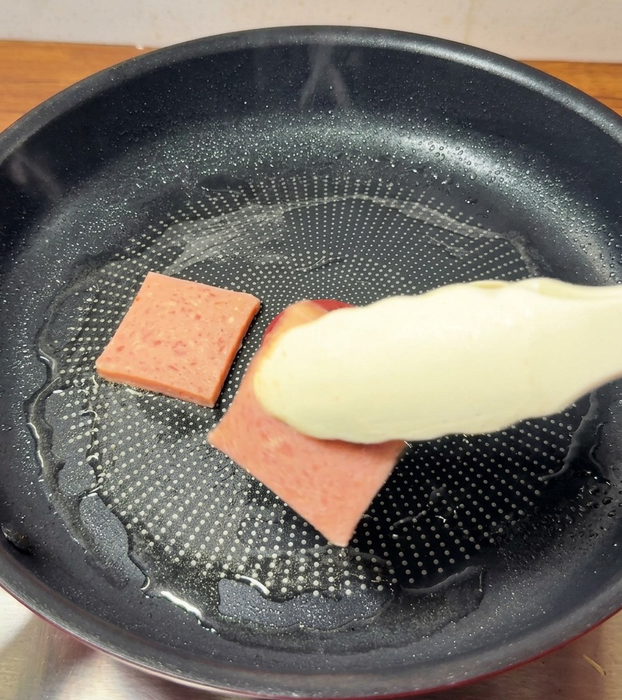 テフロン加工のフライパンでランチョンミートを焼き、トングで裏返して焼き色を確認している様子。