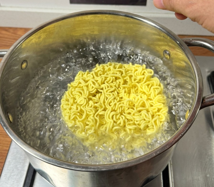 沸騰したお湯に乾燥したインスタントラーメンの麺を投入する様子。