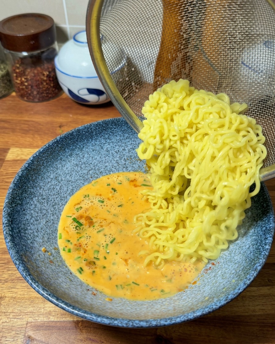 ザルで湯切りしたちぢれ麺を、用意しておいた濃厚なスープの中へ移す様子。