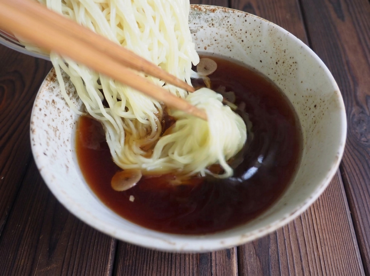 箸を使って、茹でたての麺をスープの入った丼へ優しく盛り付けている様子。
