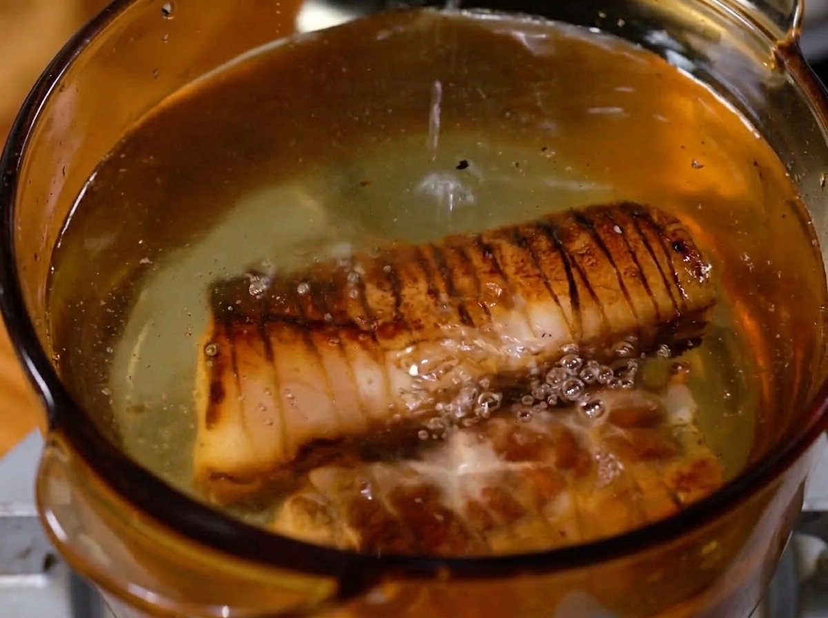 大きな鍋の中で、下茹でされている豚バラロールと香味野菜が沸騰している様子。