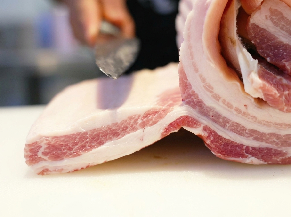 まな板の上で豚バラ肉に包丁を入れる様子