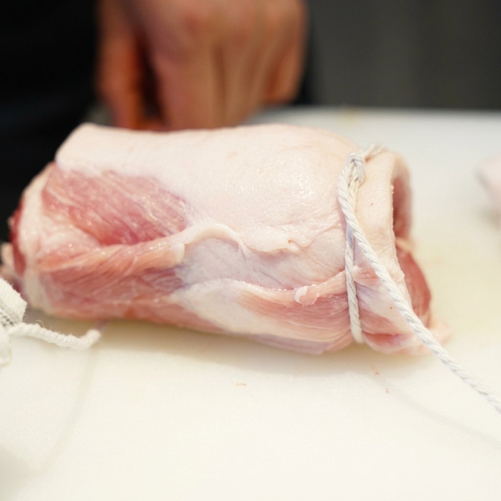 円柱状にきつく巻かれ、タコ糸で縛られた生の豚バラ肉