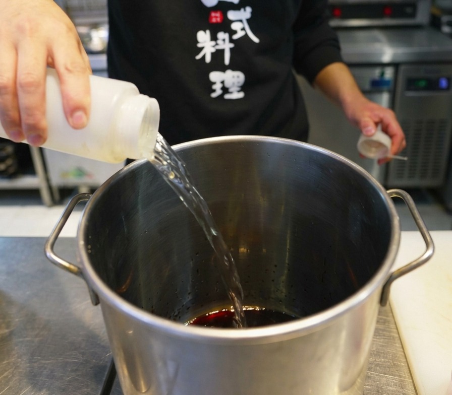 ステンレス製の大きな鍋に調味料を注ぎ入れる様子