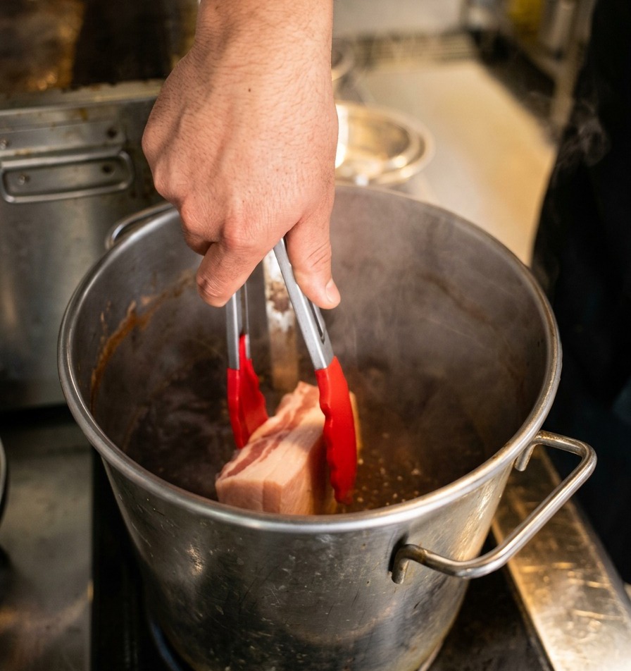 表面を焼いた豚肉を、トングでそっと濃い煮汁の鍋に入れている様子