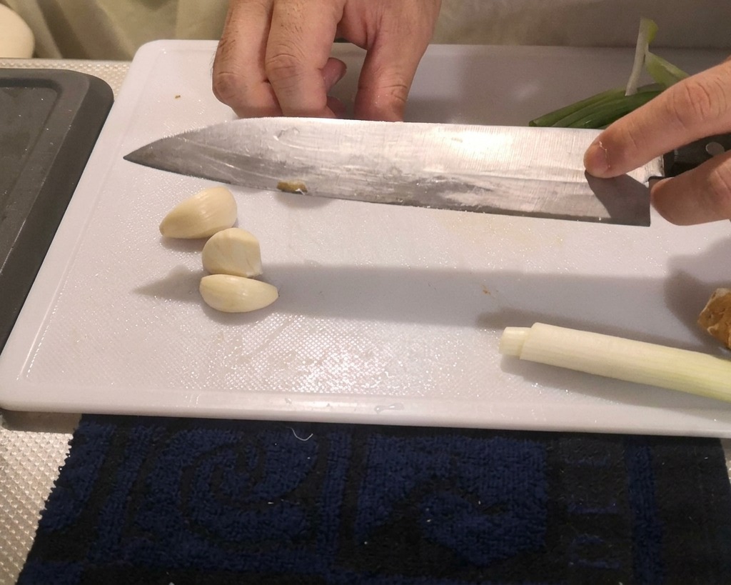 まな板の上で、皮をむいたにんにくの上に包丁の腹を当てて押し潰している様子。