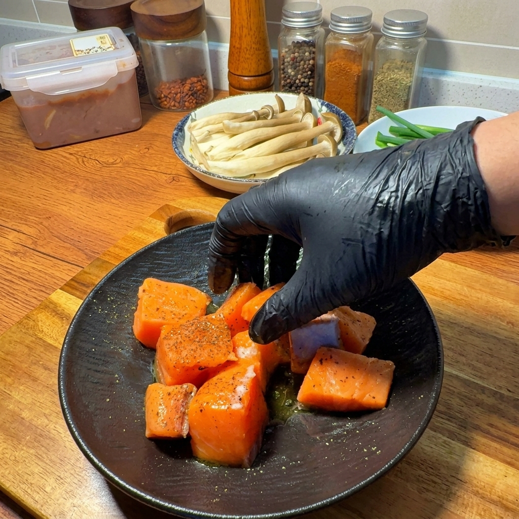 手袋をした手で、サーモンと調味料、オリーブオイルを優しく混ぜ合わせている様子。