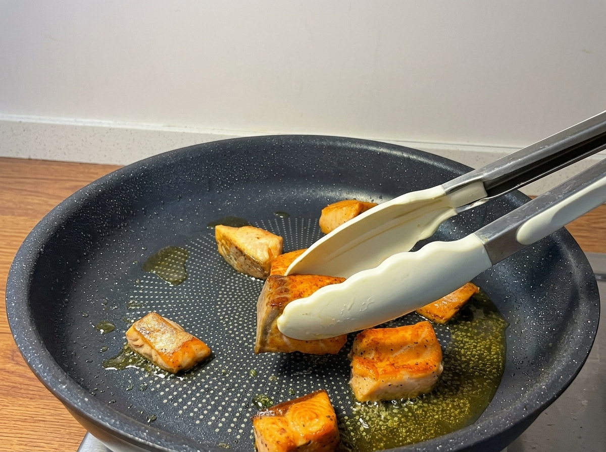 フライパンの中で、トングを使ってサーモンを裏返し、表面をこんがりと焼いている様子。