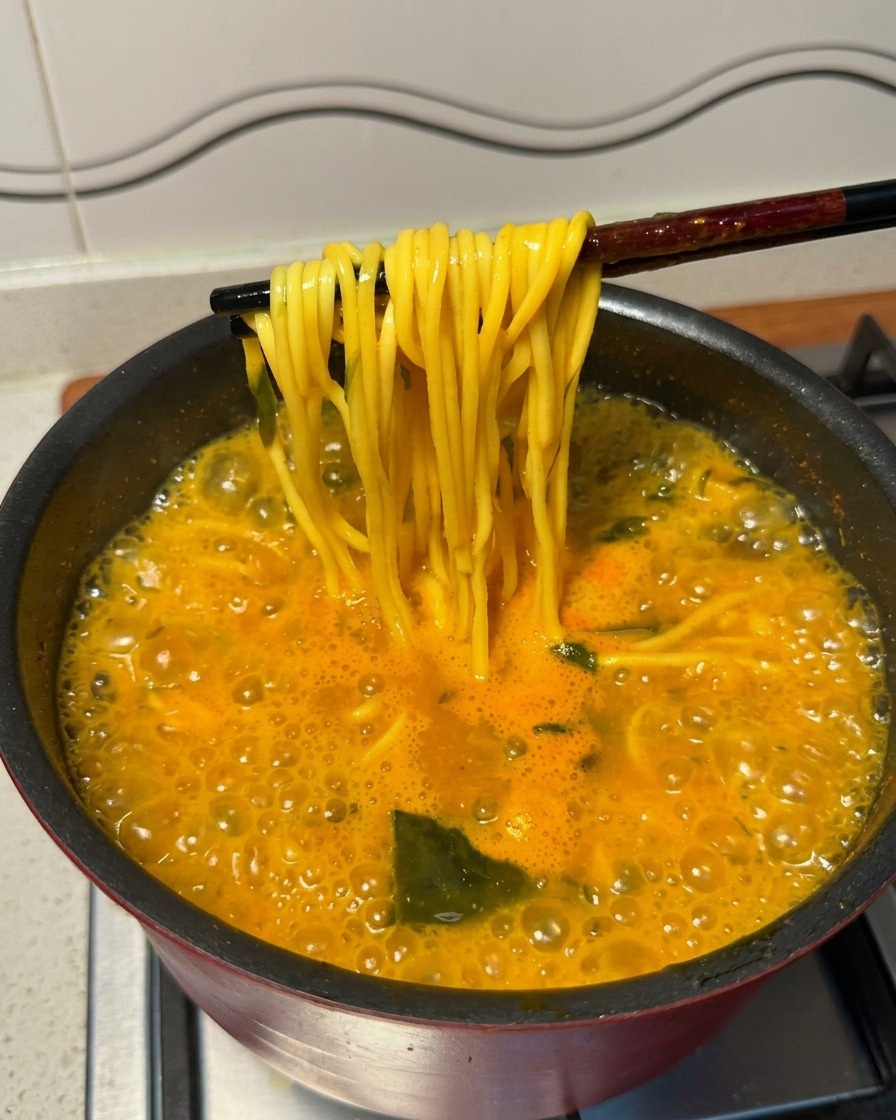 箸を使って、茹で上がった黄色い麺を熱々のスープから持ち上げている様子。