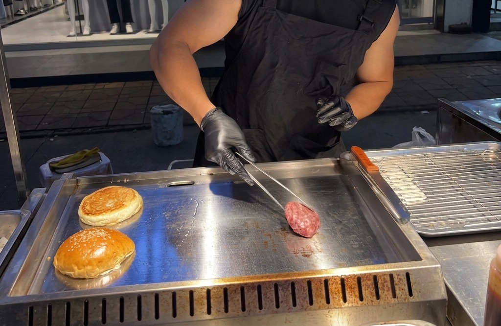 煙が上がるほど熱くなった鉄板の上に、丸めた牛ひき肉を置いている様子。