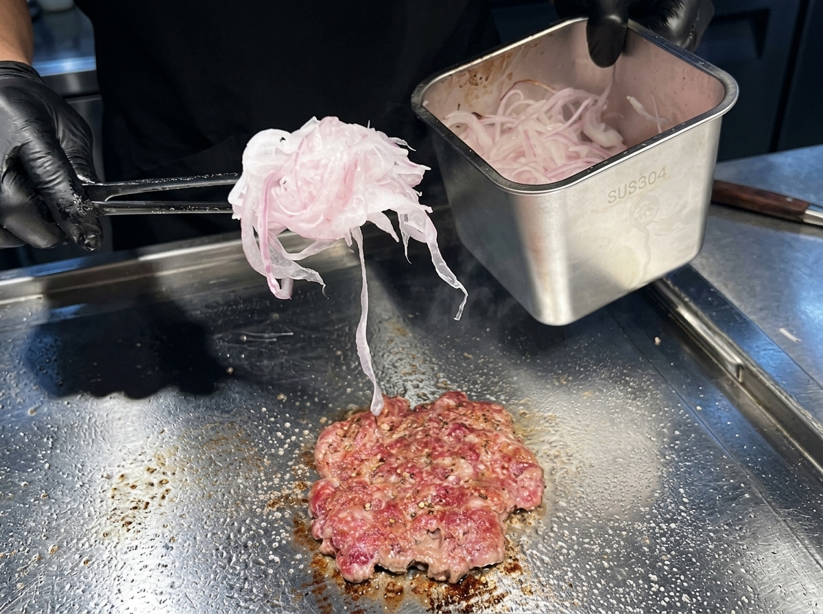 焼いている最中の肉の上に、薄切りにしたレッドオニオンをたっぷり乗せている様子。