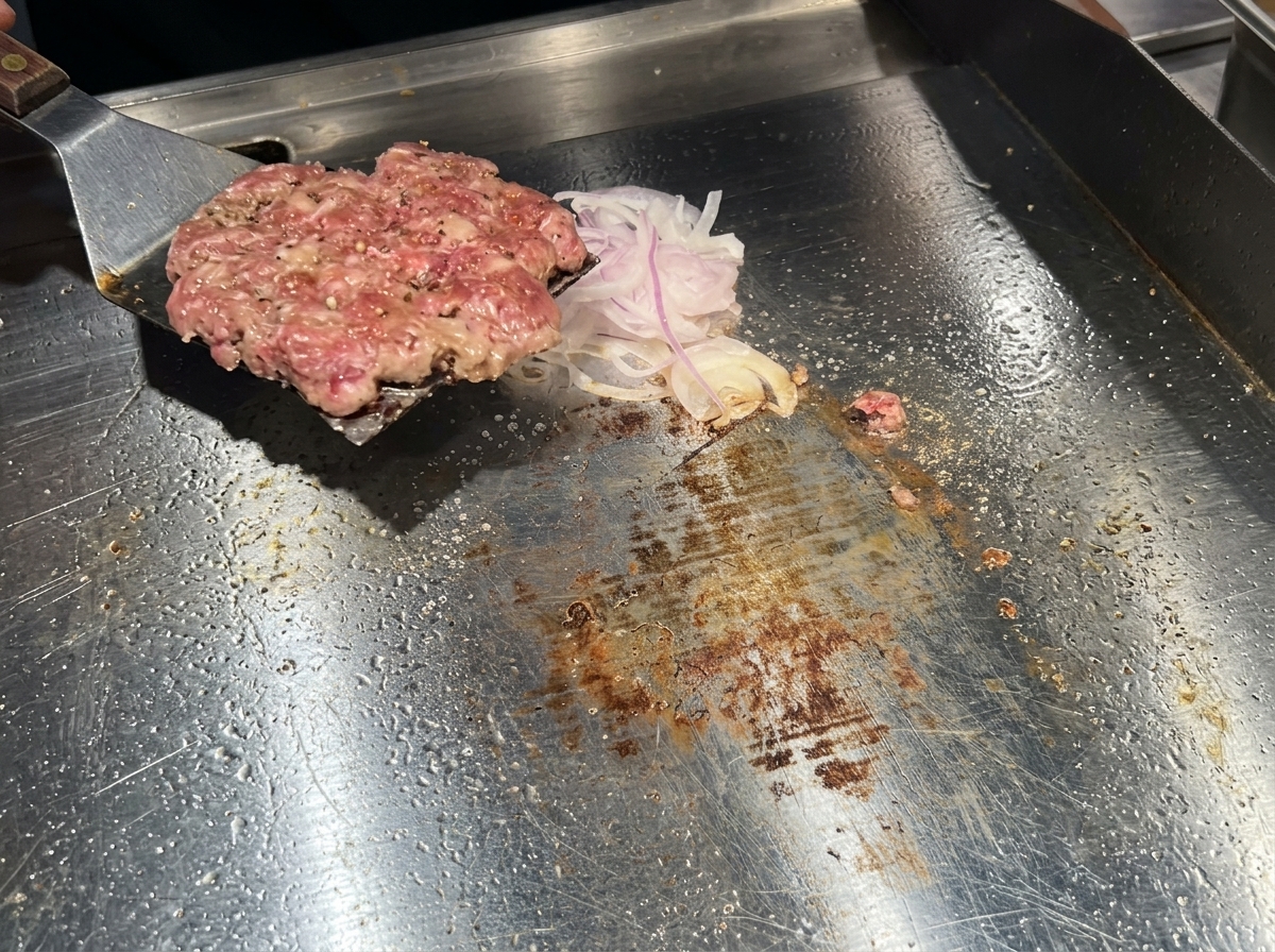 金属製のヘラを使って、焼き色のついたパティをオニオンごと裏返している様子。