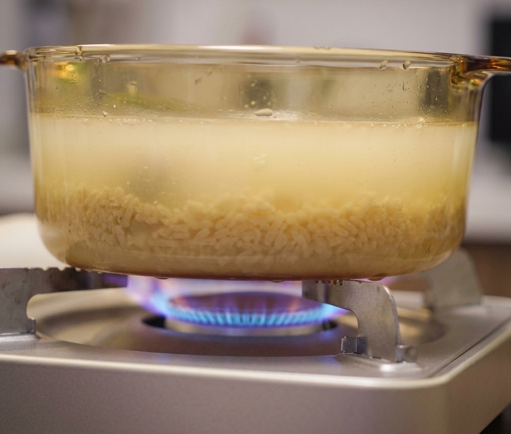 カセットコンロの上で、うっすらと黄色く色づいたスープが静かに温められている様子。