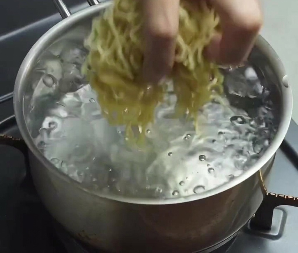 沸騰したたっぷりのお湯に、生の細ちぢれ麺を投入している様子。
