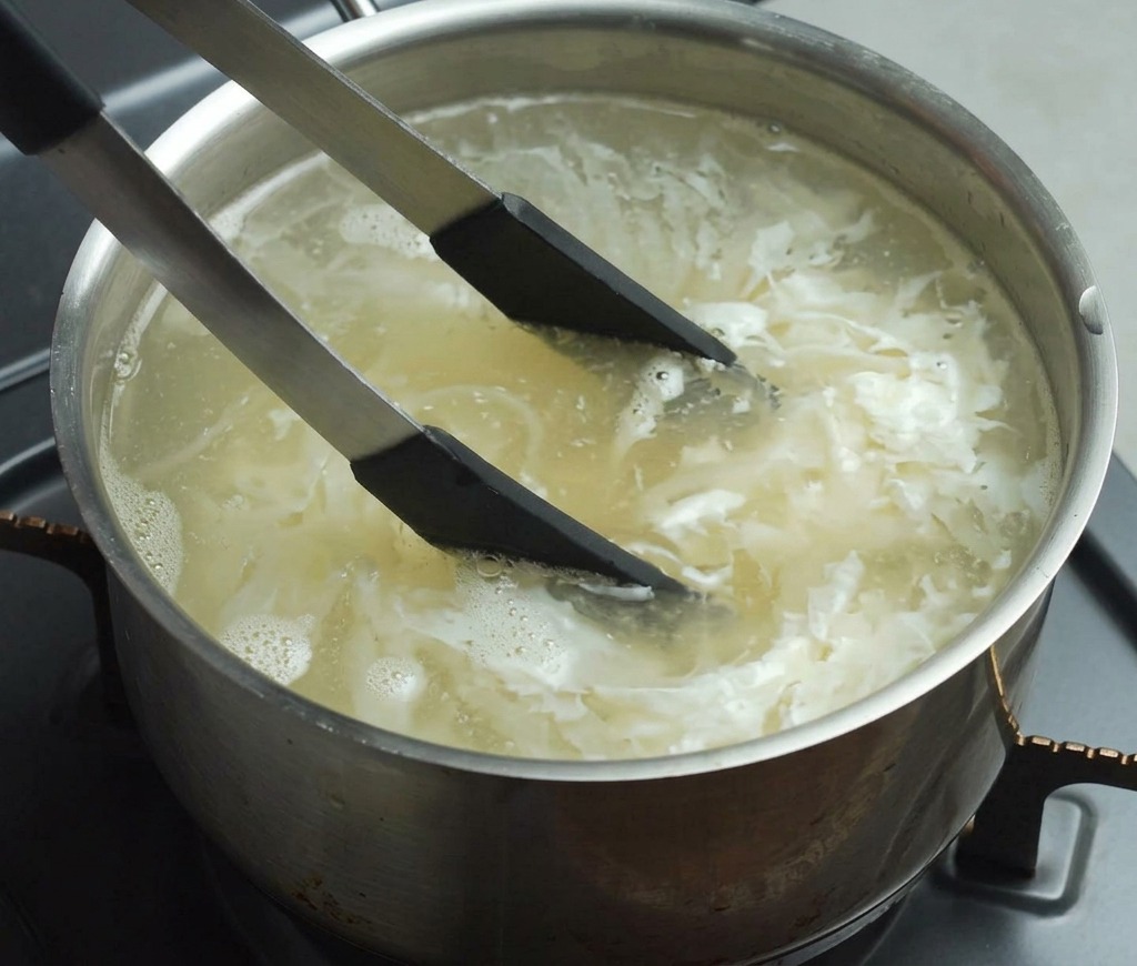 トングを使って、沸騰したお湯の中で麺をほぐしながら茹でている様子。