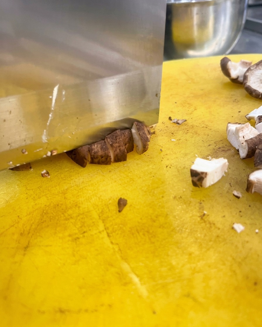 黄色いまな板の上で、茶色のしいたけを小さな立方体に刻んでいる様子。