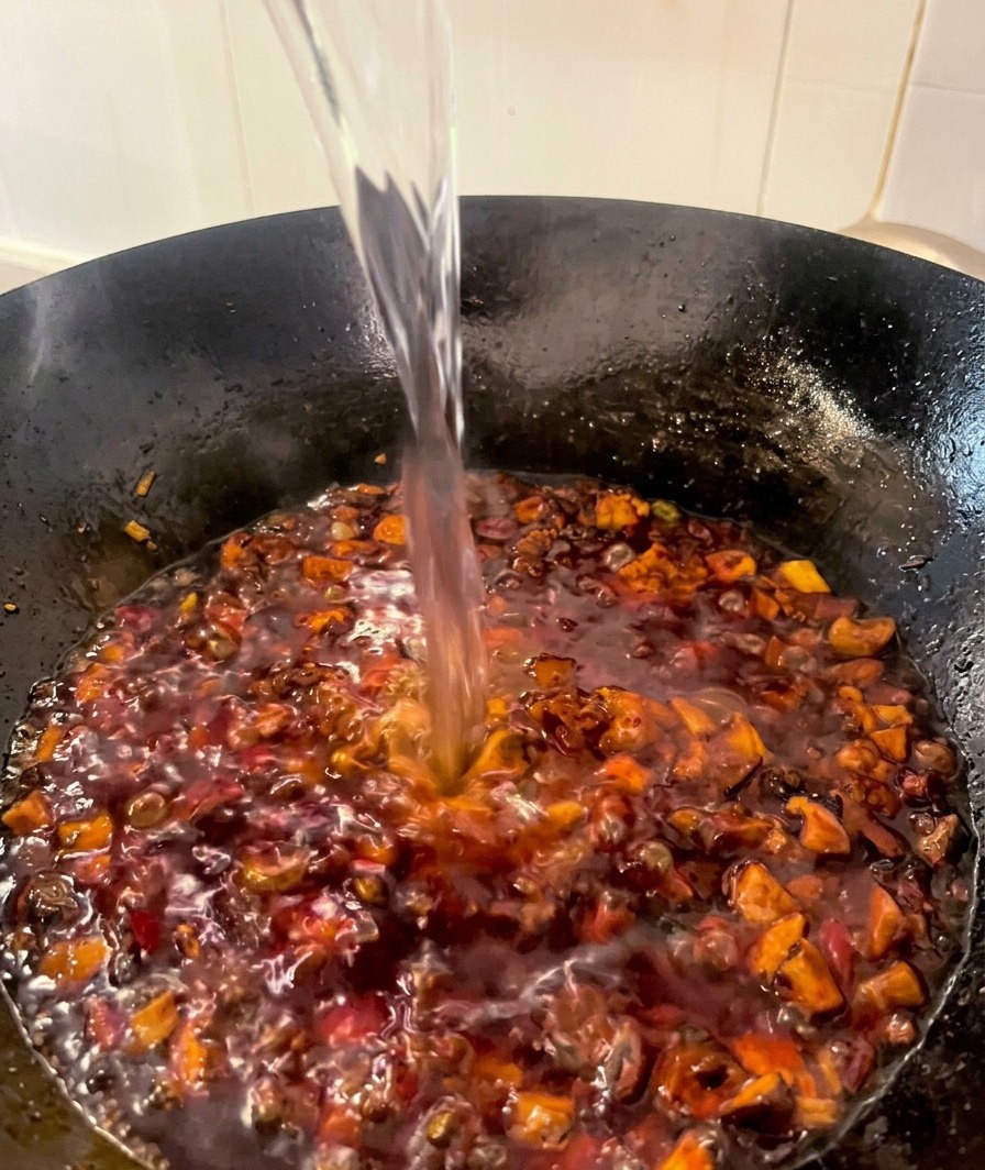 鶏肉としいたけが入った赤いソースに、水を注ぎ入れている様子。