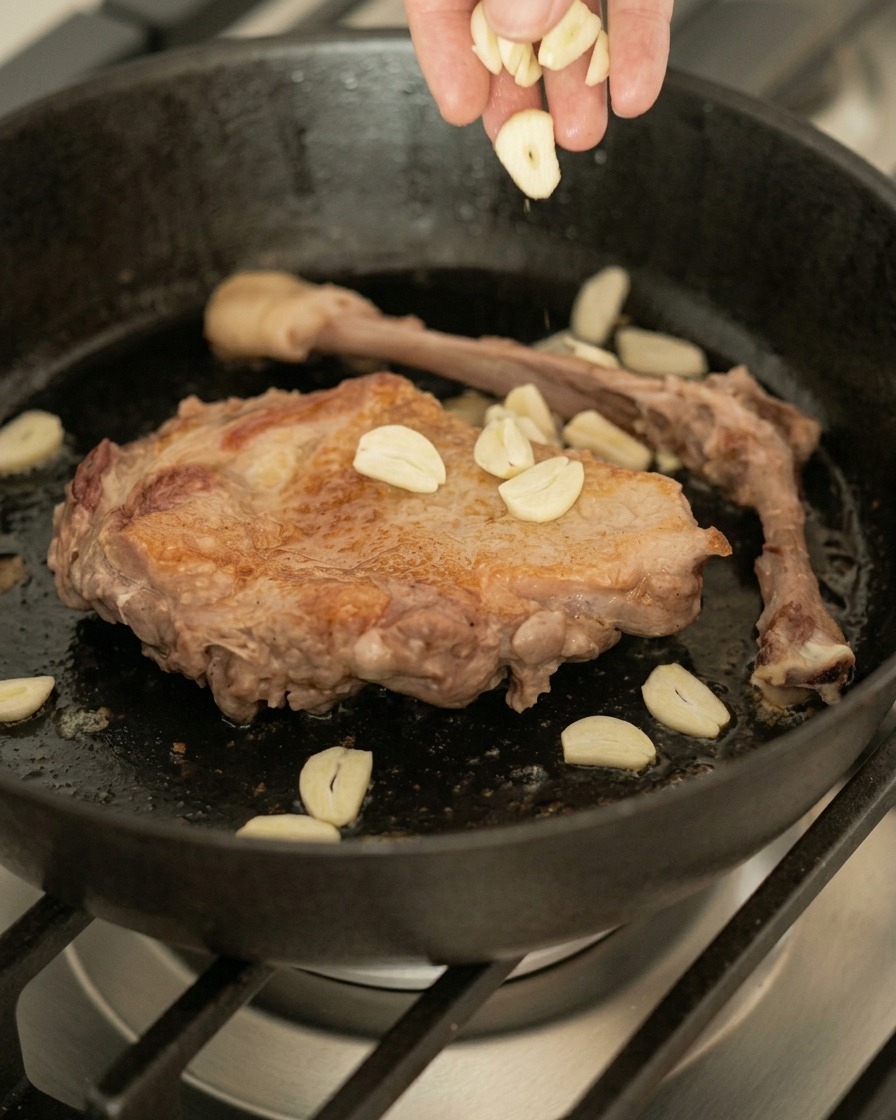 焼いた鴨肉が入ったスキレットに、スライスしたにんにくを加える様子。