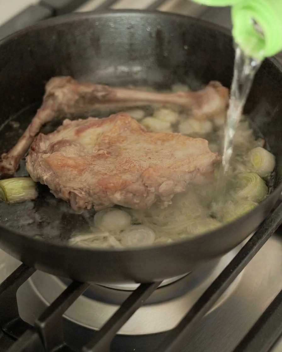 鴨肉とネギが入ったスキレットに、ボトルから酒を注ぐ様子。