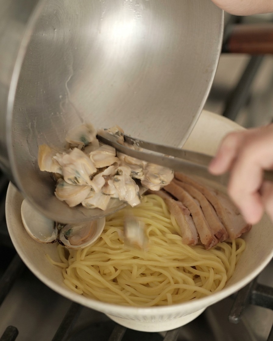 鴨肉と麺の上に、火を通したあさりを盛り付ける様子。