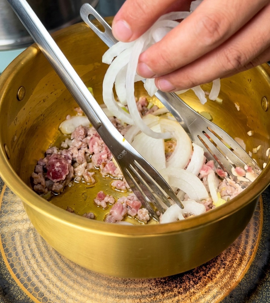 炒めたひき肉と香味野菜が入った鍋に、スライスした玉ねぎを加える手元。