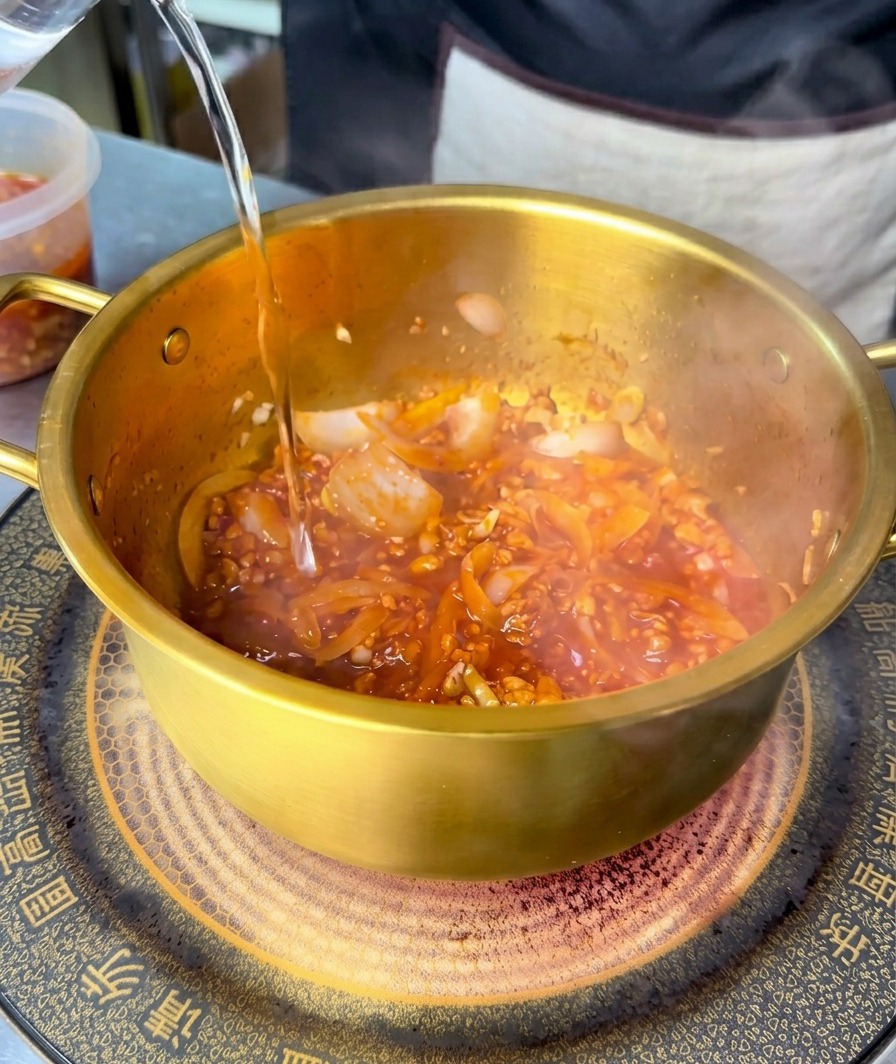 赤い炒め物のベースが入った鍋に、透明な水を注いでいる様子。