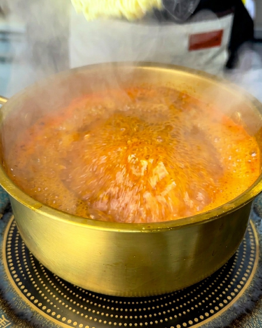沸騰した赤いスープにインスタントラーメンの乾麺を沈めている様子。