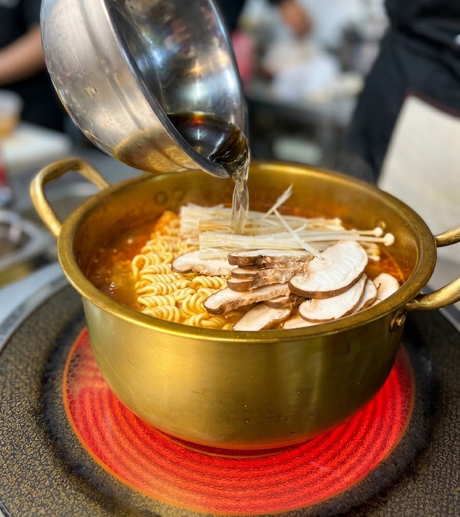 麺とスープが入った鍋にエビやムール貝などの海鮮を入れている様子。