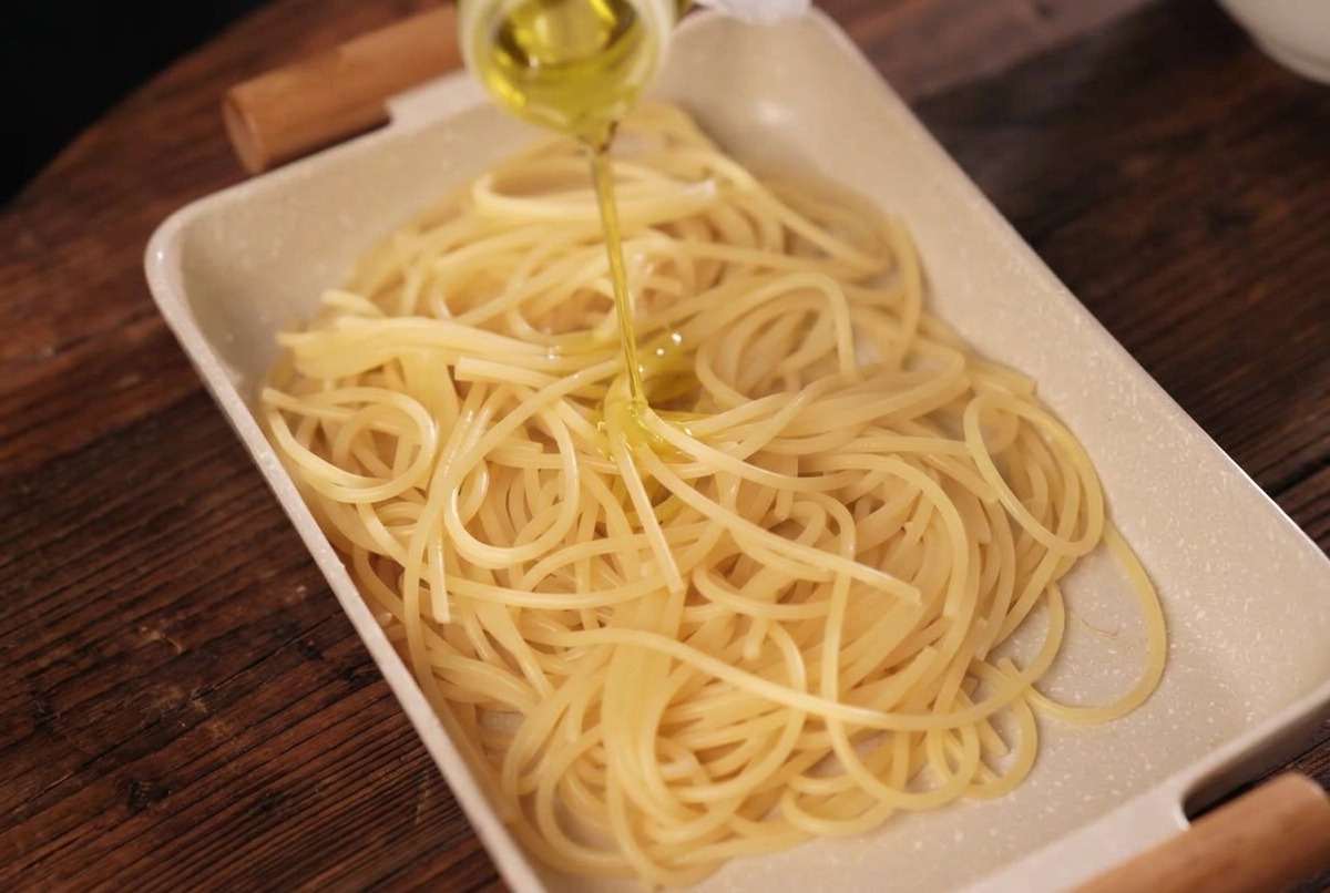 茹で上がったパスタにボトルからオリーブオイルを回しかける様子