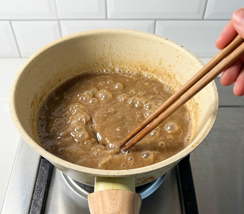 コンロの上で茶色のスープが沸騰し、菜箸で混ぜている様子。