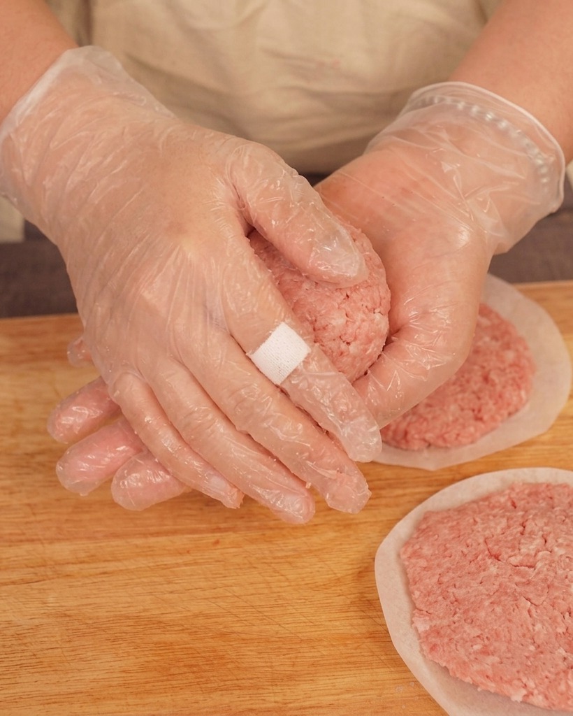 手袋をした手で挽き肉を丸め、手のひらで叩きつけるようにしている様子。