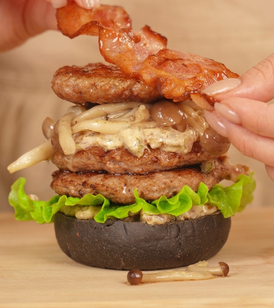 バーガーの最上部にベーコンをのせて仕上げる様子。
