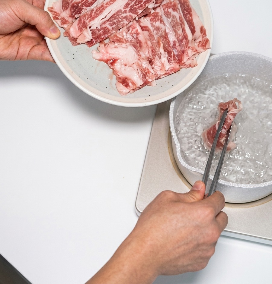 沸騰したお湯の中に、トングを使って薄切りの牛霜降り肉を入れ、素早く湯通ししている様子。