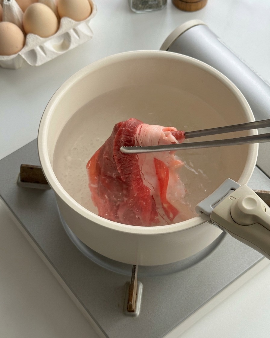 沸騰した鍋のお湯に菜箸を使って生の牛薄切り肉を入れ、湯通ししている様子。