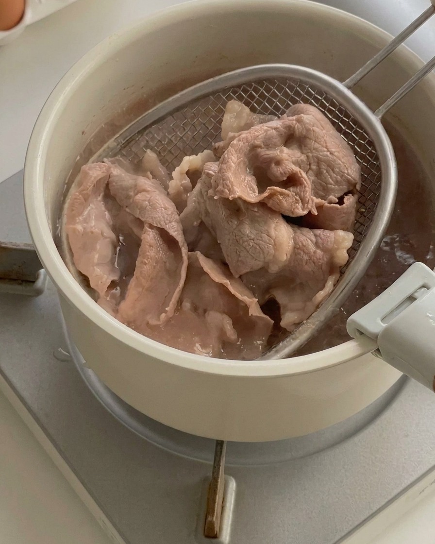 あみ杓子を使って、沸騰したお湯から茹で上がった牛薄切り肉を引き上げている様子。
