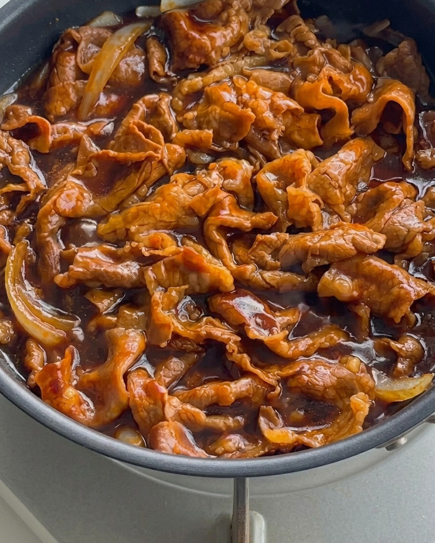 フライパンの中で、濃くツヤのあるタレが泡立ちながら、牛薄切り肉と玉ねぎにしっかり絡んでいるクローズアップ。