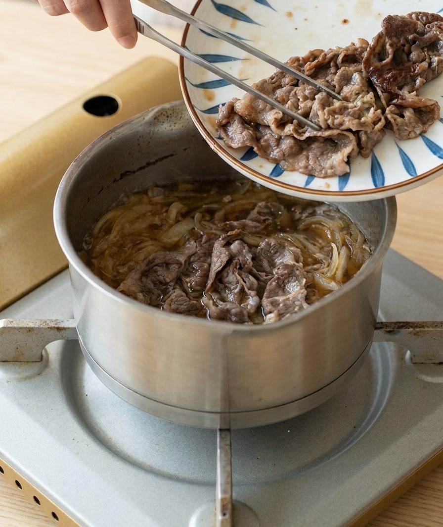 焼き色のついた牛肉を、柄物の皿から玉ねぎとタレが煮立つ鍋へと移し入れる様子