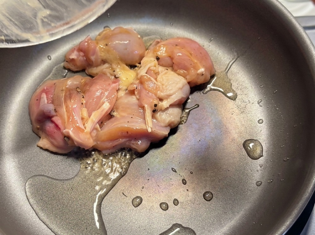 薄く油をひいた熱いフライパンで、下味をつけた鶏肉の切り身を焼いている様子。