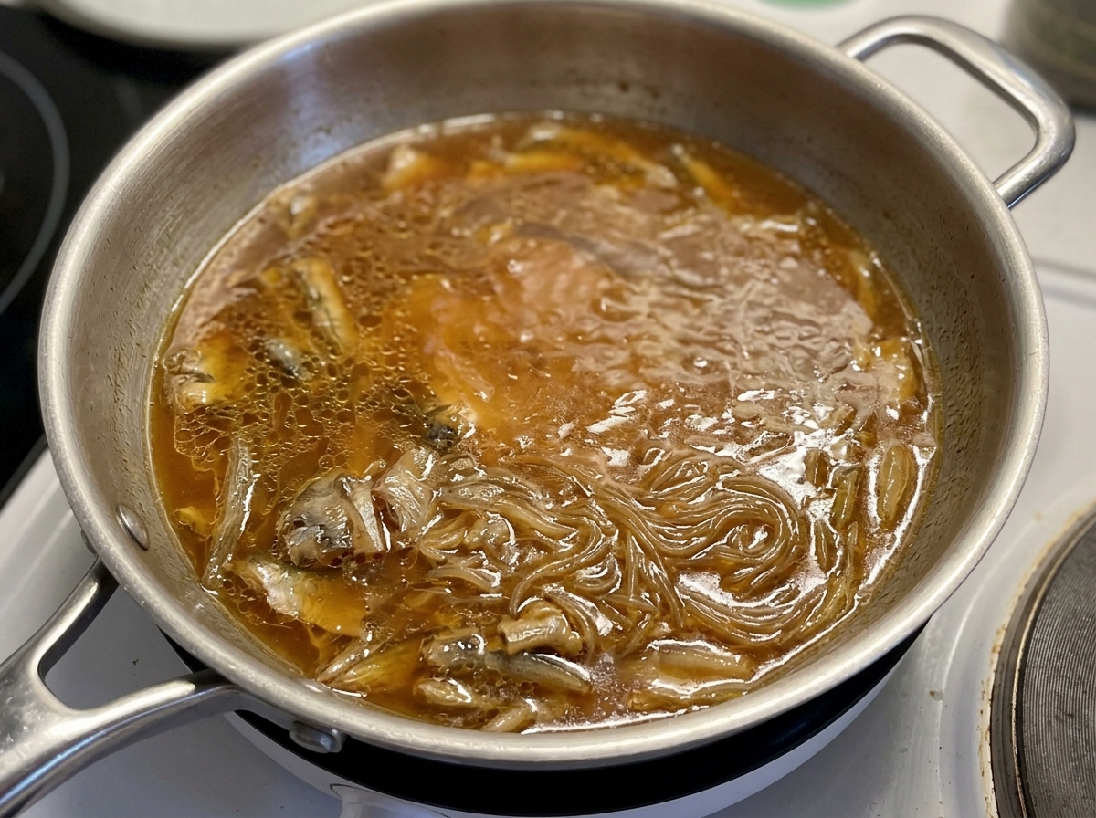 鶏肉と玉ねぎが濃い茶色のタレで煮込まれているフライパンに、ガラスの蓋をかぶせようとしている様子。