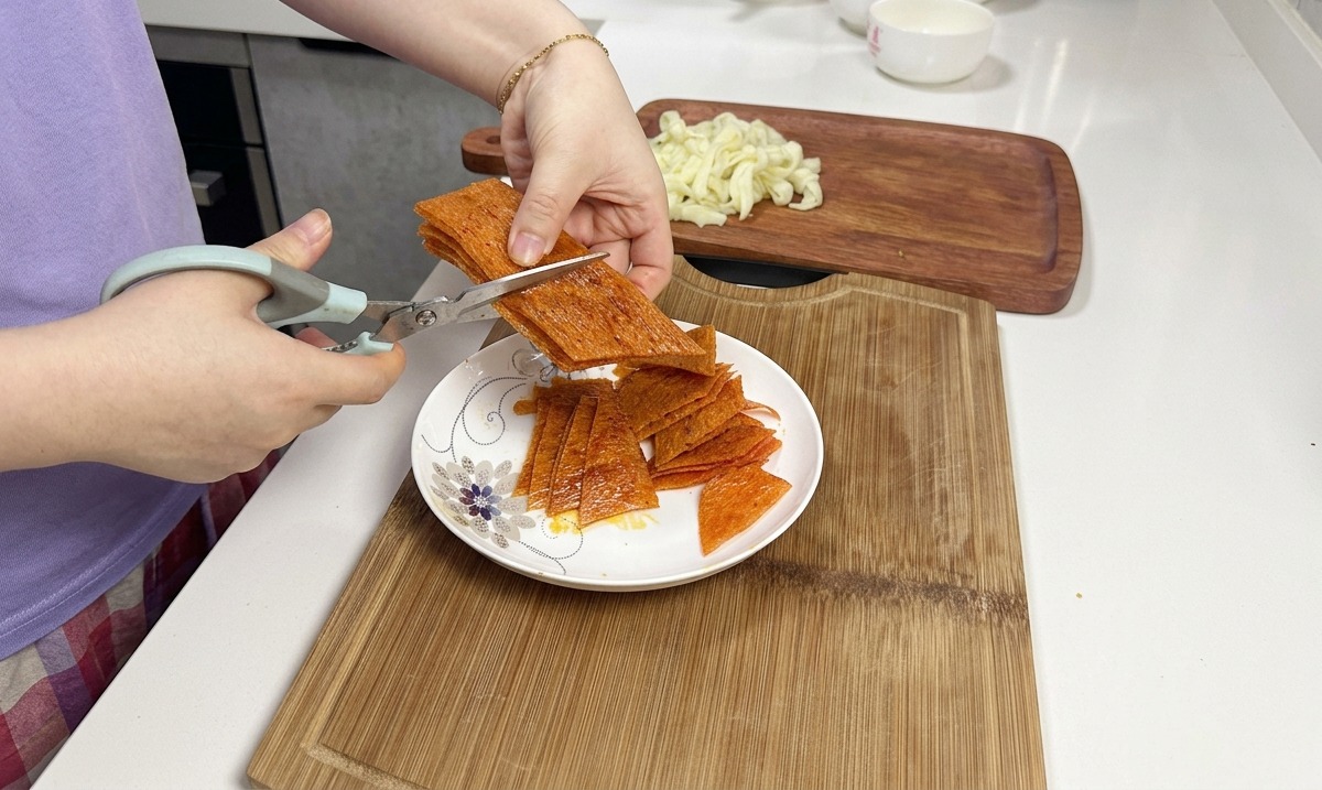 白いお皿の上で、重ねられたオレンジ色のスパイシーな辣条の束を、キッチンバサミを使ってカットしている様子。