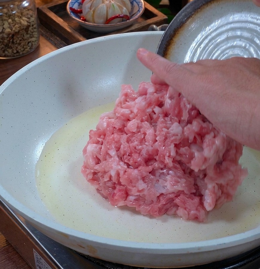 薄く油をひいた白いセラミックのフライパンに入れられる、新鮮なピンク色の豚ひき肉